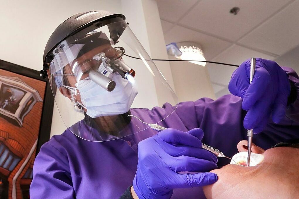 Một bác sĩ nha khoa tại Seattle đeo khẩu trang, tấm chắn giọt bắn khi khám răng cho bệnh nhân vào tháng 6. Ảnh: AP