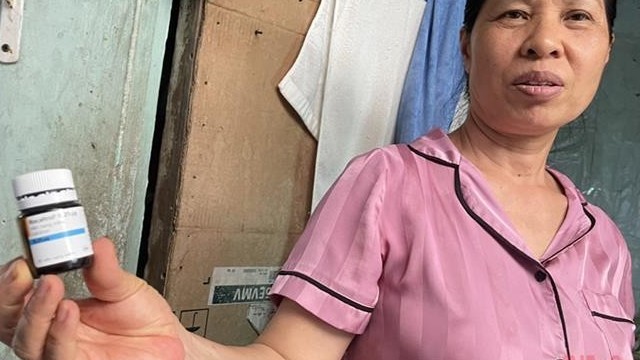 Bà Mai Thị Hường cùng lọ thuốc canxi dạng viên dùng tạm thay thế trong khi hết thuốc. (Ảnh: SƠN BÁCH)